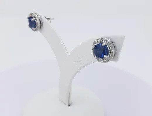 A pair of sapphire and diamond circular cluster earrings in white gold, on an earring stand, against a white background