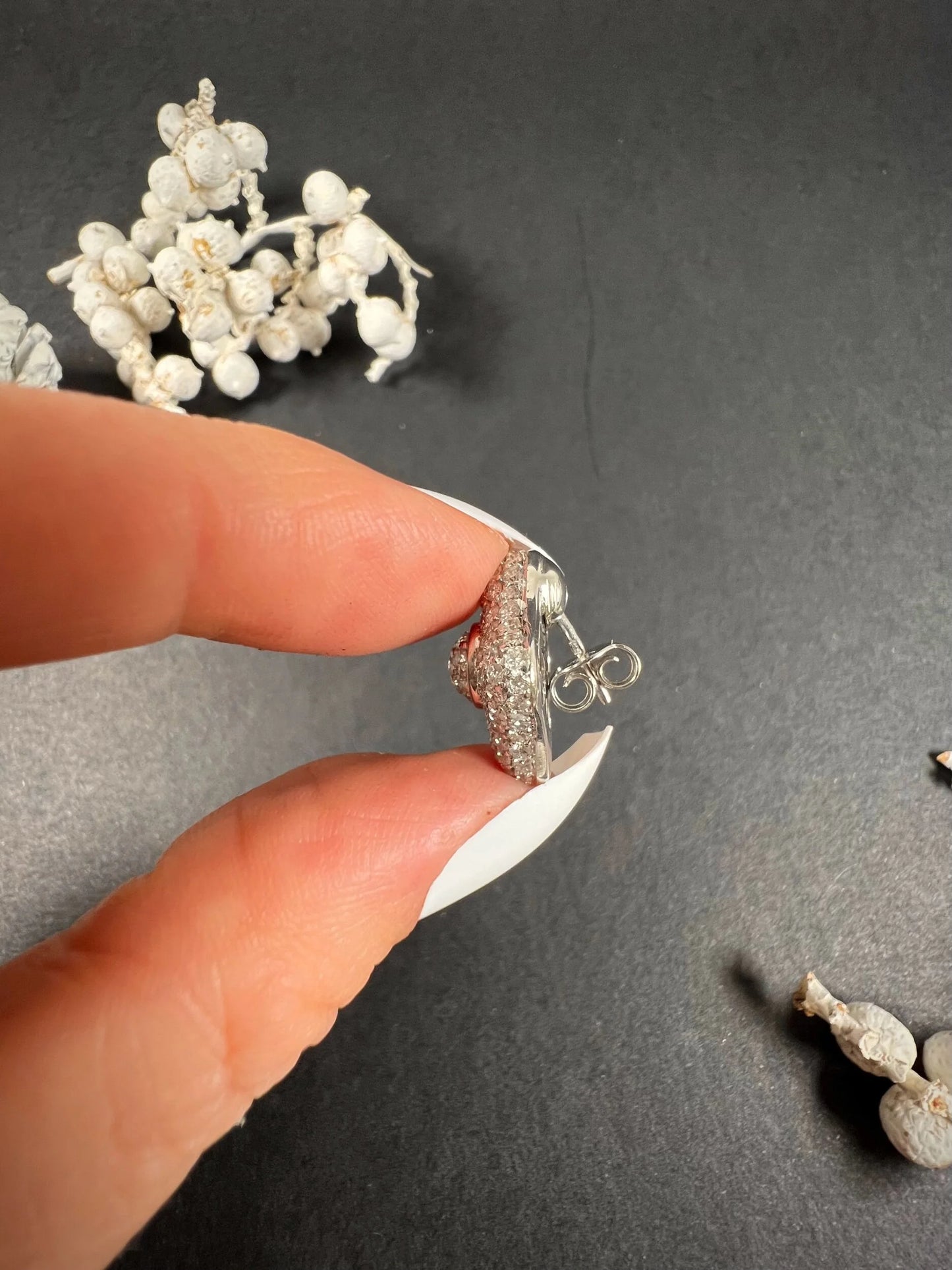 A white gold diamond earring, held in a hand
