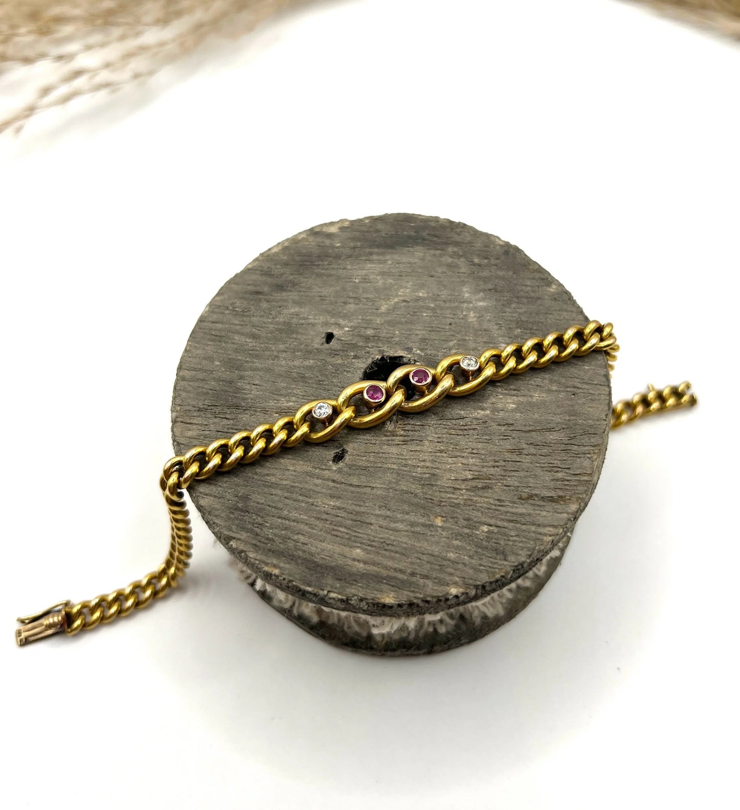 A yellow gold curb link bracelet with rubies and diamonds, on a wooden spool