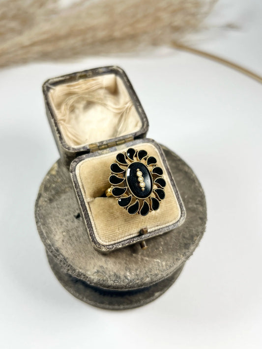 A black onyx and seed pearl fancy halo cluster ring in yellow gold, in a ring box