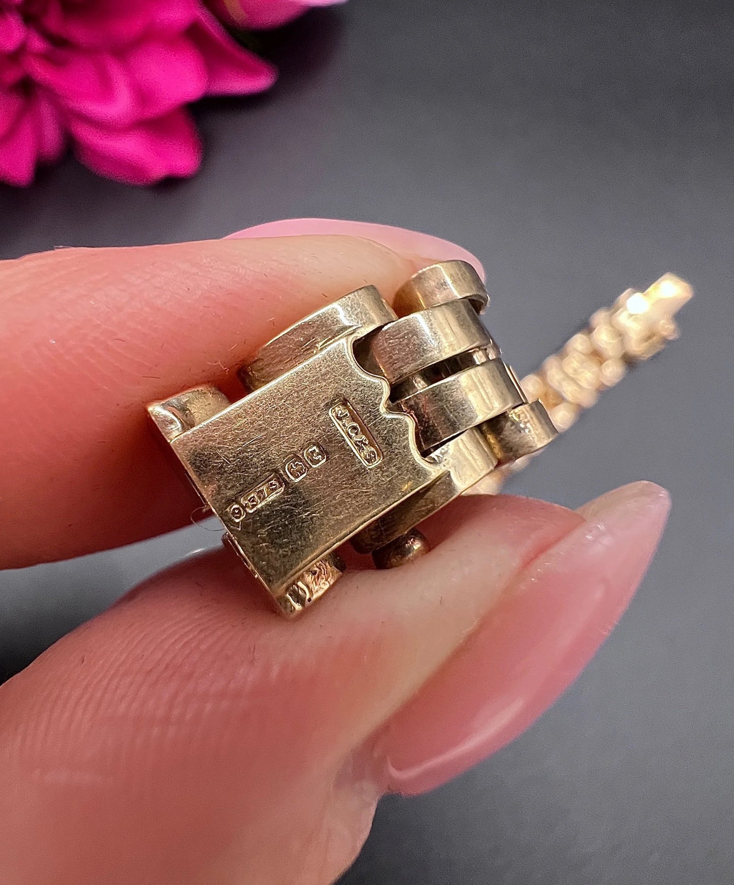 Close-up of 9 carat gold hallmarks on a yellow gold bracelet, held in a hand