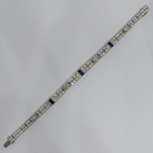 An Art Deco line bracelet set with four marquise cut diamonds to an encrusted border of early brilliant cut and baguette cut diamonds with sapphire accents. These bright, white diamonds are estimated to weigh a total of 4.80ct.