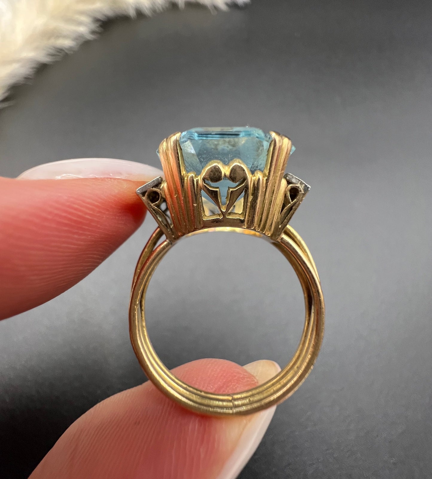 An octagonal cut aquamarine and diamond cocktail ring in yellow gold, held in a hand