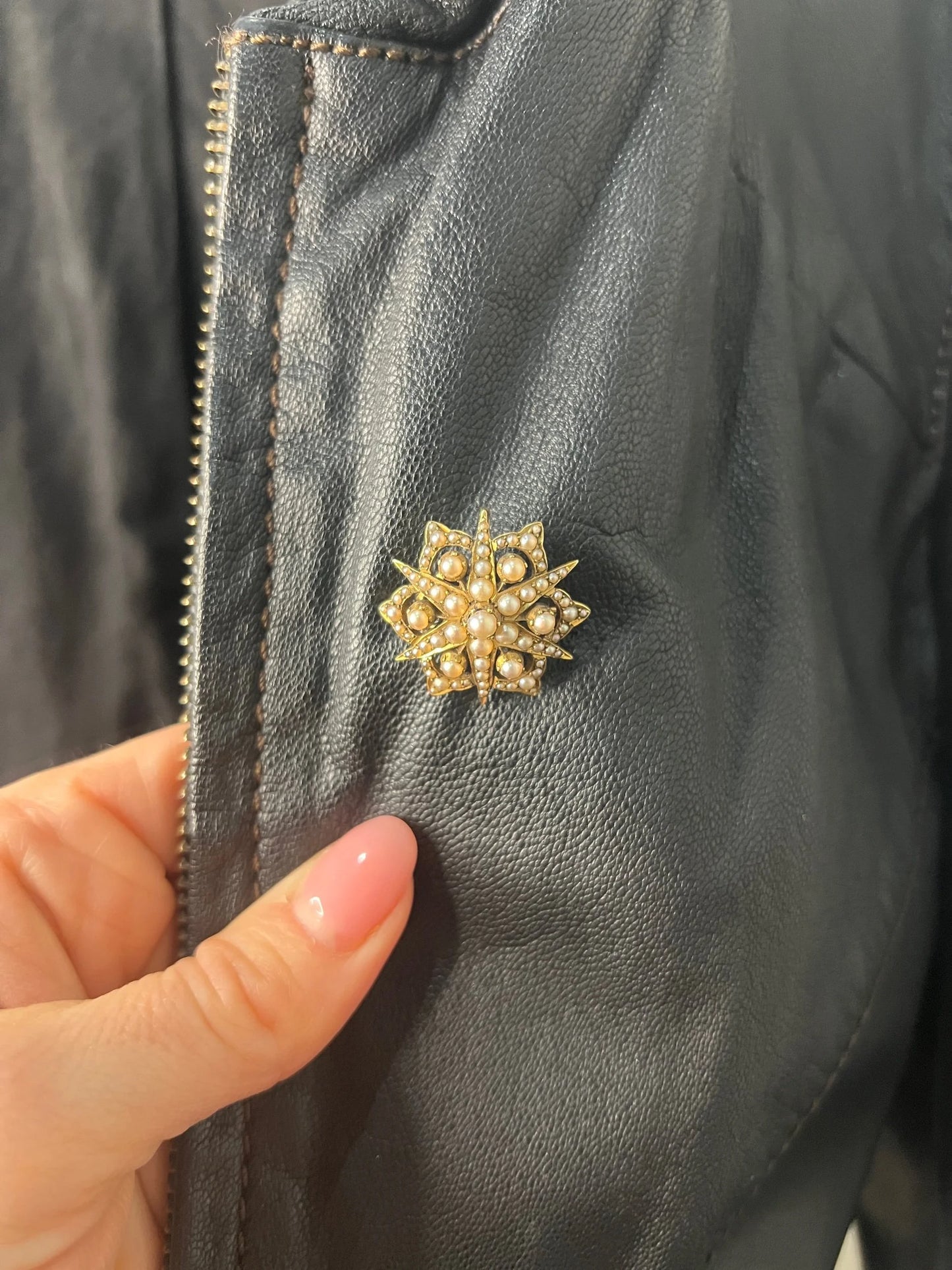 A yellow gold brooch/pendant with pearls in the shape of a star, modelled on a black jacket