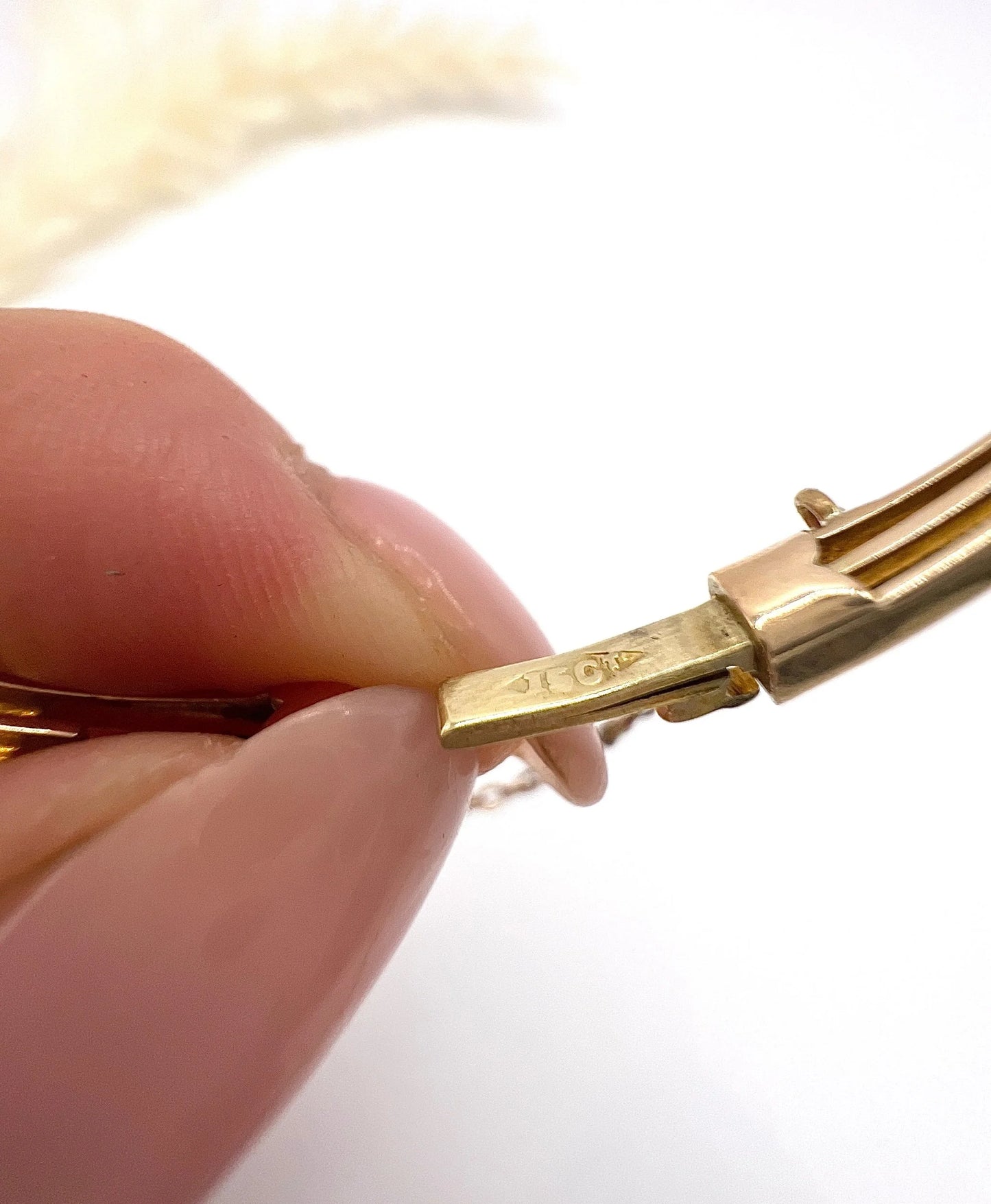 A close-up of a gold bracelet clasp stamped 15CT, held by a hand