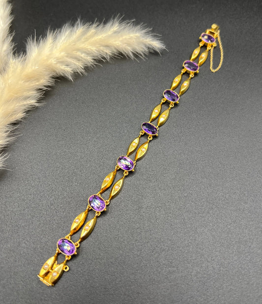 A yellow gold amethyst and pearl double row bracelet, laid flat on a black background