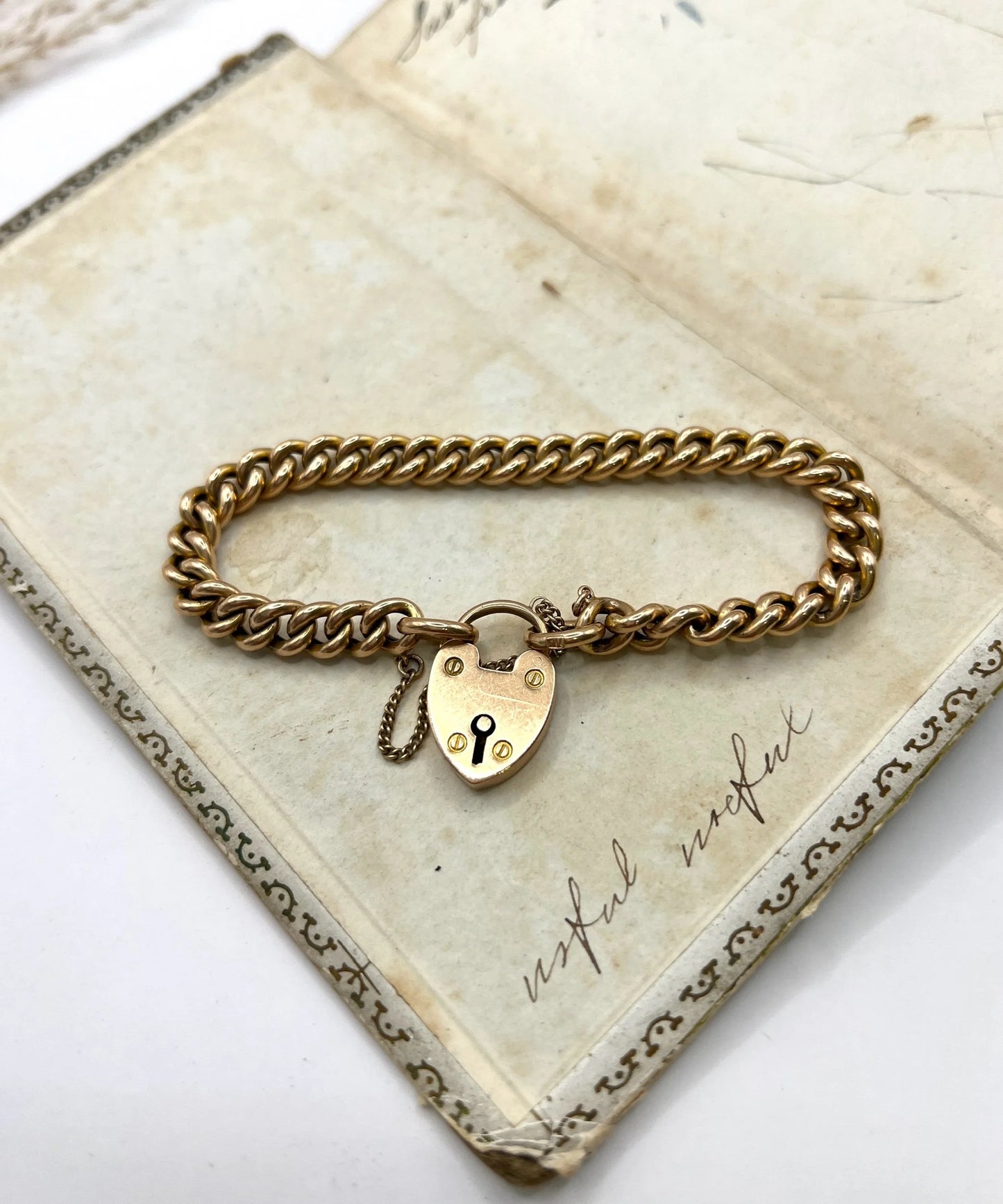 A gold curb link bracelet with heart shaped padlock, laid on an antique box