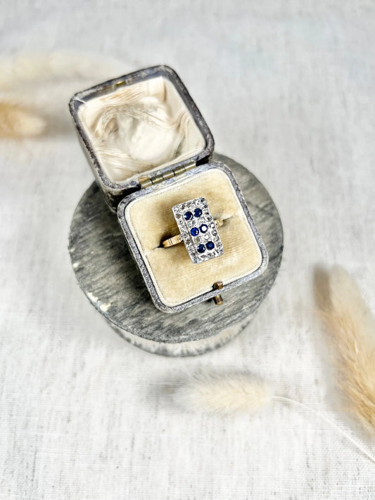 A rectangular shaped ring with sapphires and diamonds in yellow and white gold, in a box