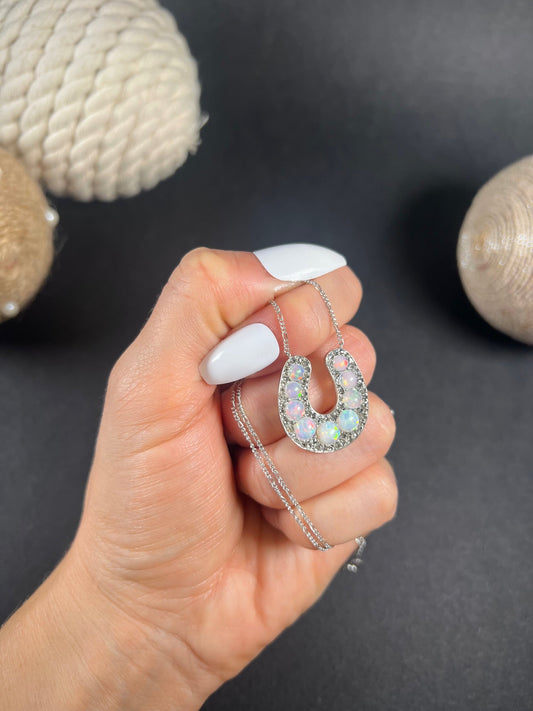 An opal and diamond horseshoe pendant with integrated chain, held in a hand