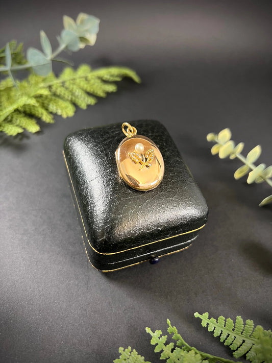 A yellow gold oval locket with a pearl set flower motif