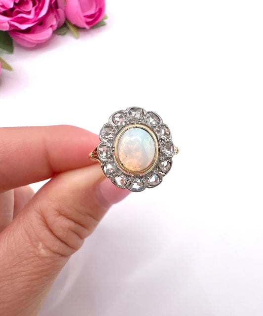 An oval opal and diamond cluster ring in yellow and white metal, held in a hand