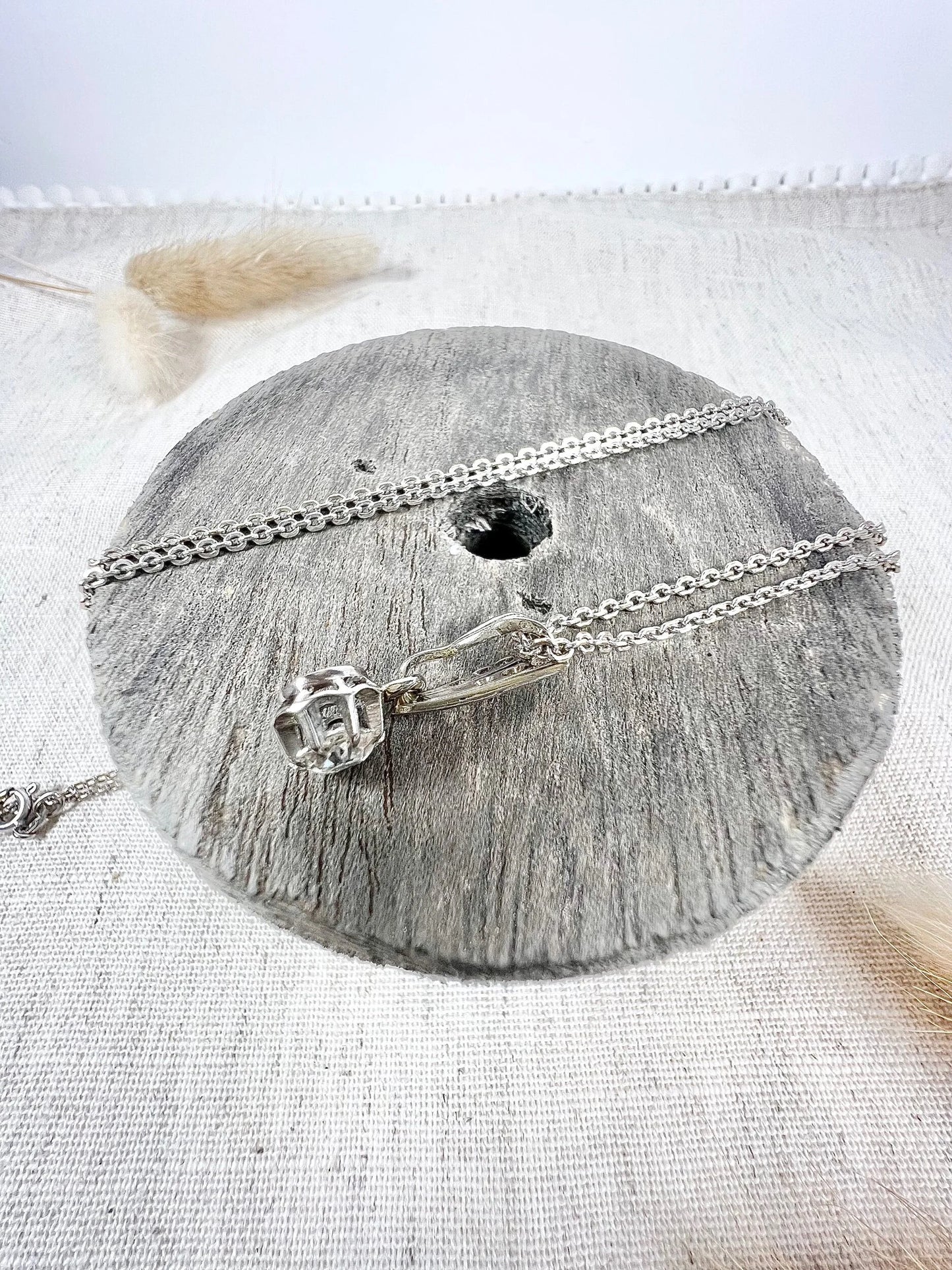 An old cut diamond pendant in white metal with a matching chain, on a circular wooden object