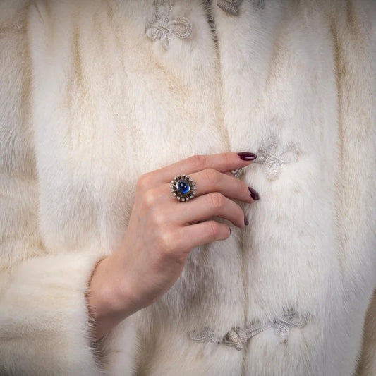 A cabochon blue sapphire and diamond ring in platinum, modelled on a hand in front of a fur coat
