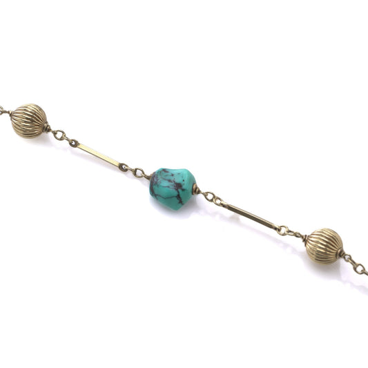 A yellow gold long chain necklace with turquoise nuggets, on a white background