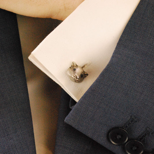 A white gold badger head cufflink with sapphire eyes, on a white shirt cuff against a blue suit