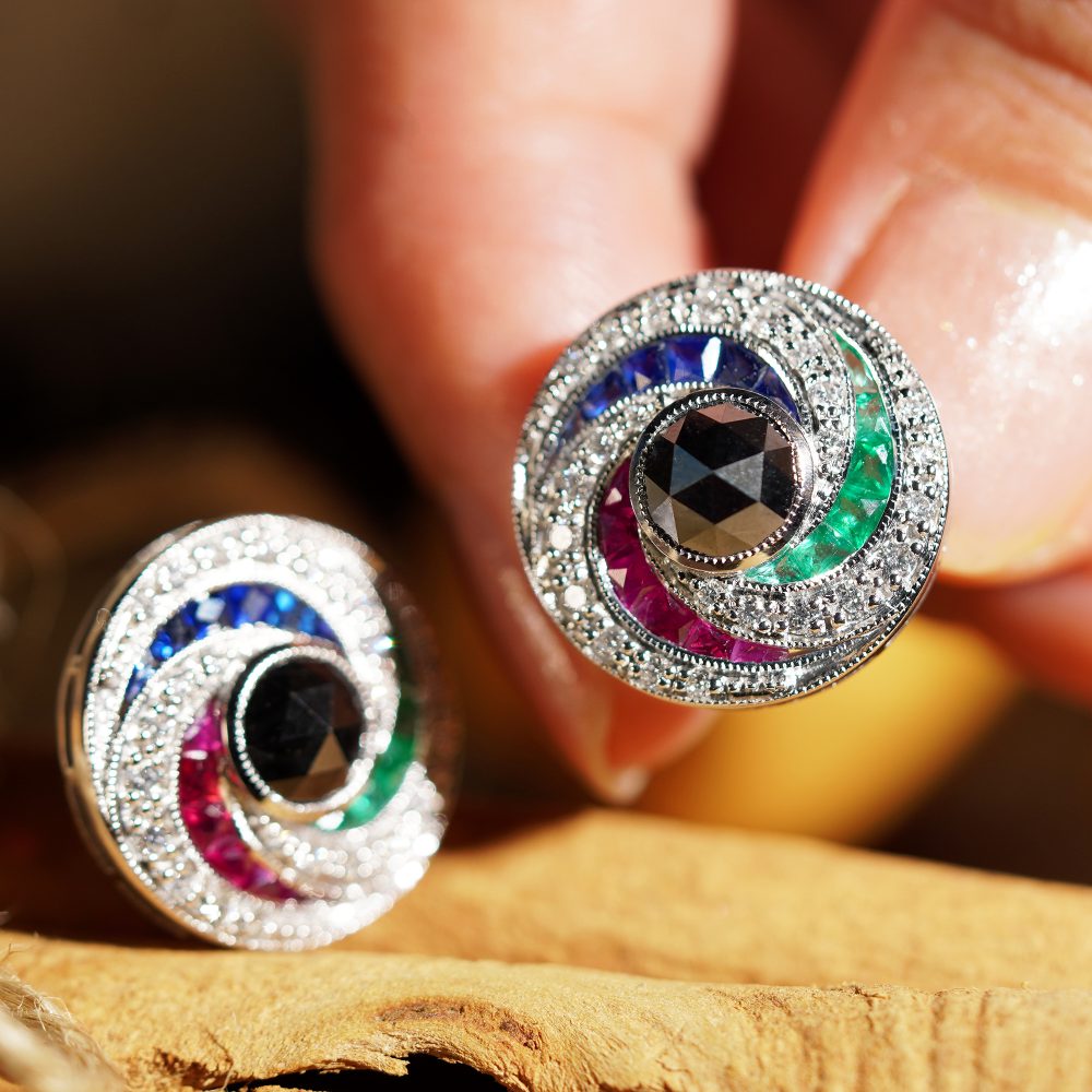 Black Diamond and Multi Gemstone Swirl Cluster Stud Earrings, round rose-cut black diamonds surrounded by French-cut rubies, sapphires and sparkling white round brilliant-cut diamonds in pin-wheel design in 14ct white gold