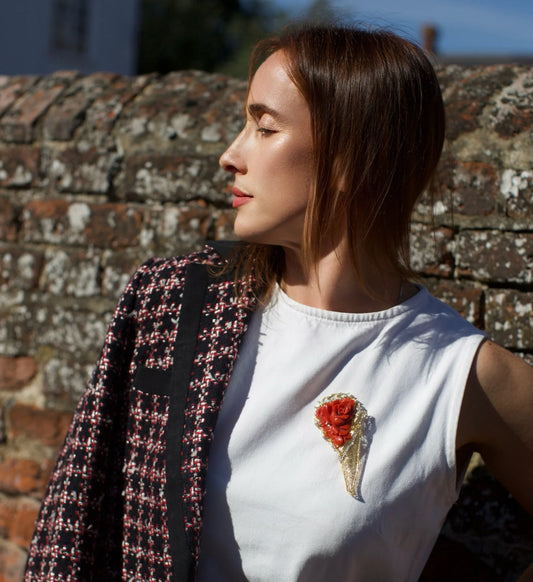 A woman wearing a red coral, diamond and yellow gold large statement brooch, against a brick wall