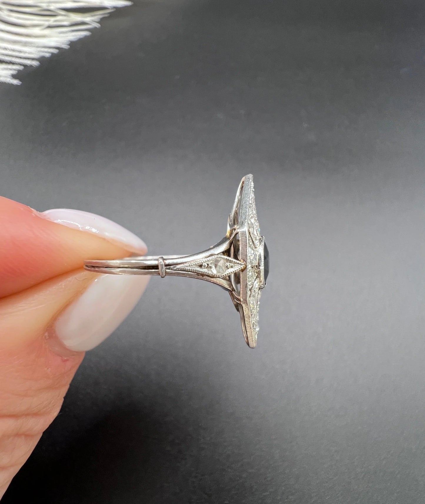 A navette shaped cluster cocktail ring with a sapphire centre surrounded by diamonds, in platinum, held in a hand