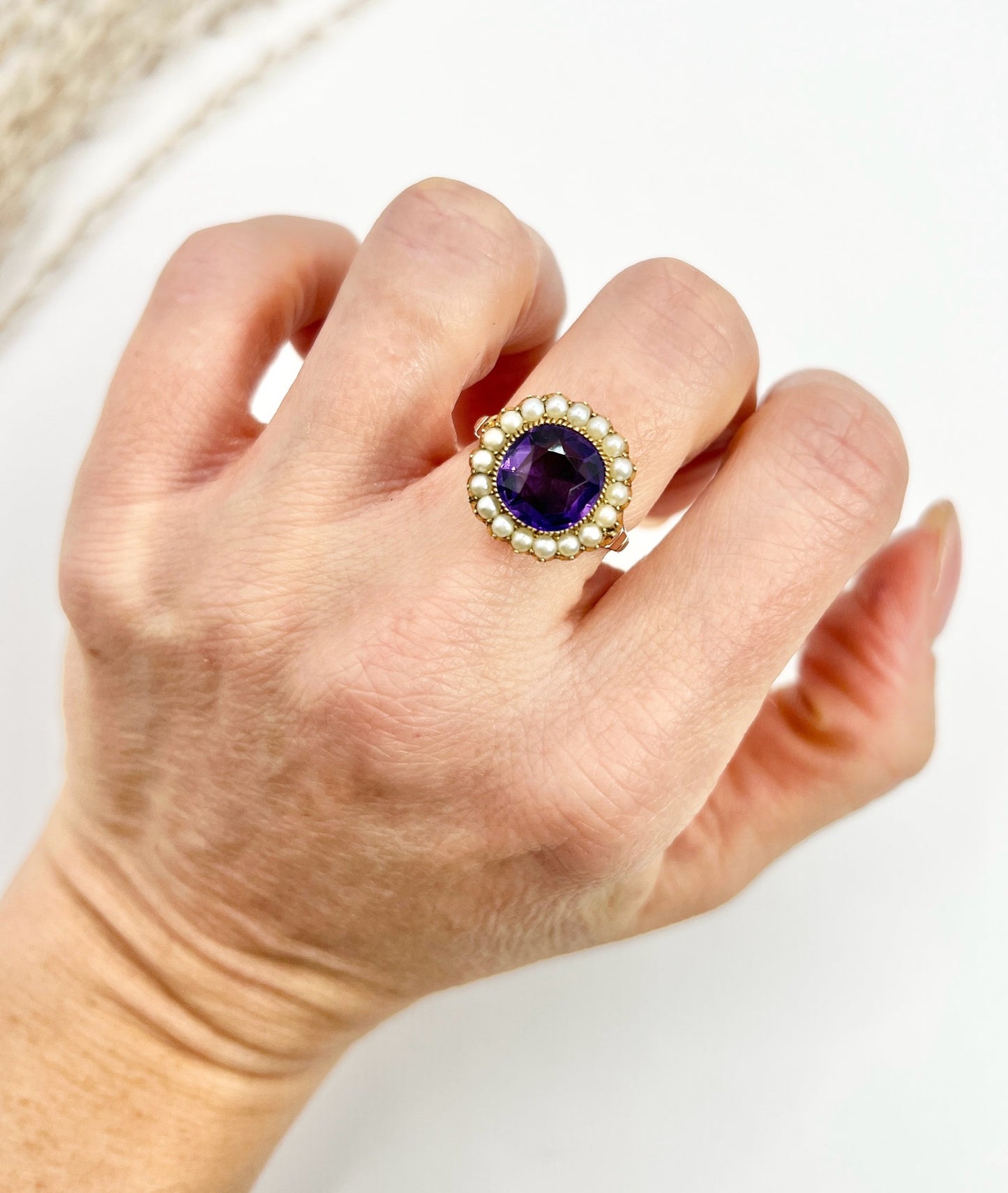 A cushion shaped amethyst cluster ring with a pearl border, in yellow gold, modelled on a hand