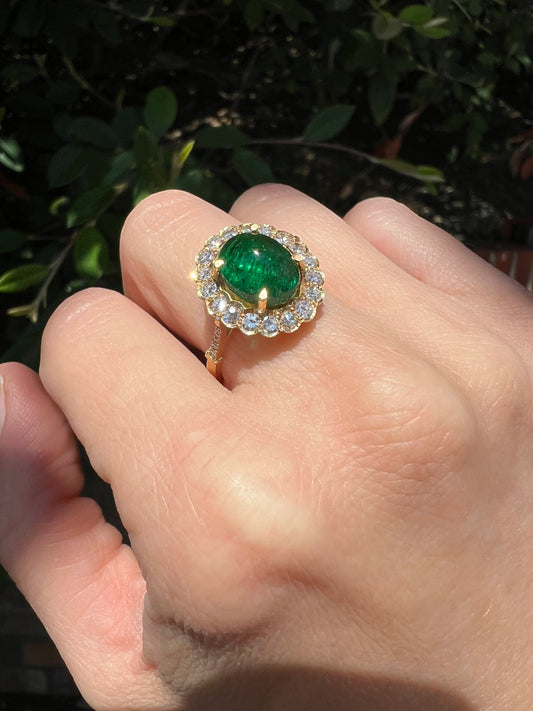 A yellow gold ring with an oval emerald surrounded by round diamonds, modelled on a hand
