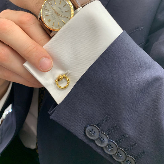 A yellow gold rope design cufflink in a white shirt cuff against a blue suit