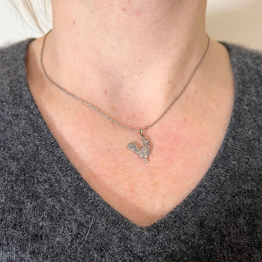 A rose cut diamond rooster pendant with a ruby eye, modelled on a white metal chain