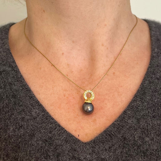 A black pearl pendant with a yellow gold bale set with diamonds, modelled on a gold chain