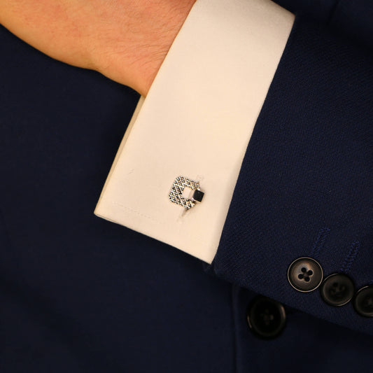A textured white gold cufflink in a white shirt cuff against a dark blue suit