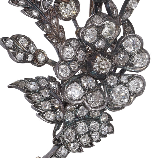 A decorative floral brooch set with old cut diamonds, in silver and gold, on a white background