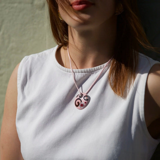 A pink enamel circular pendant with diamonds on a pink cord, modelled by a woman wearing a white top