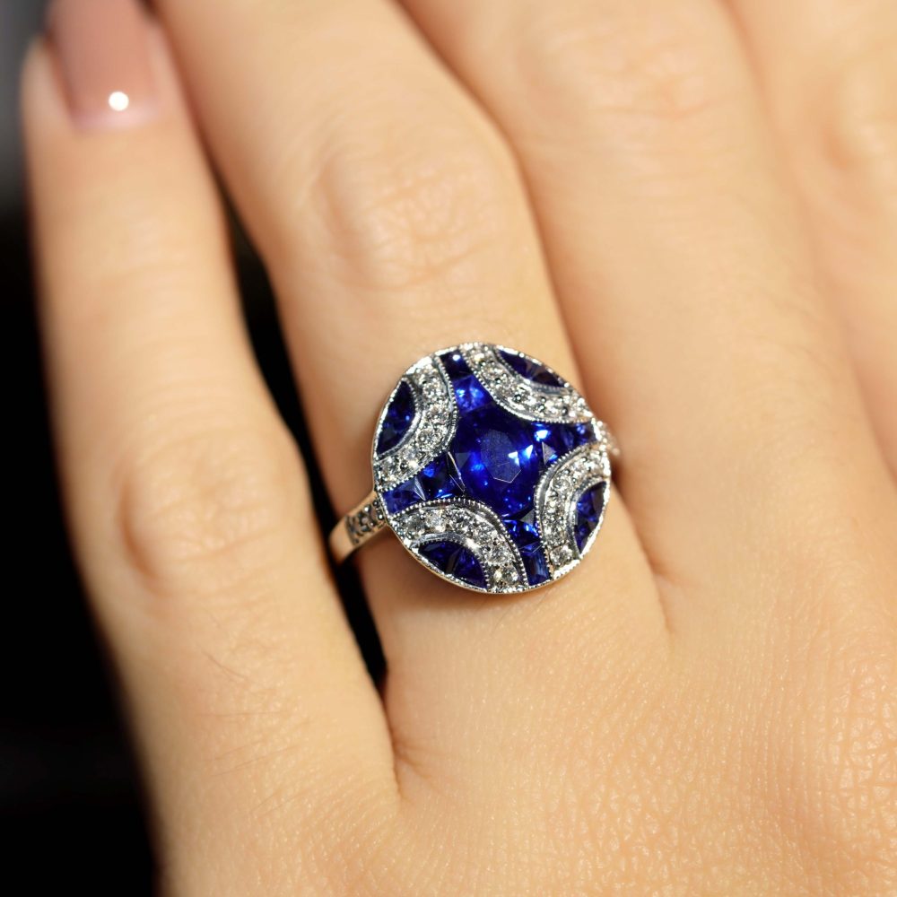 1.10ct Oval Sapphire and Diamond Geometric Cluster Dress Ring, 1.10ct oval-cut sapphire adorned by 1.25cts French cut sapphires with round brilliant diamond lines on each corner in 18ct white gold with millegrain edging