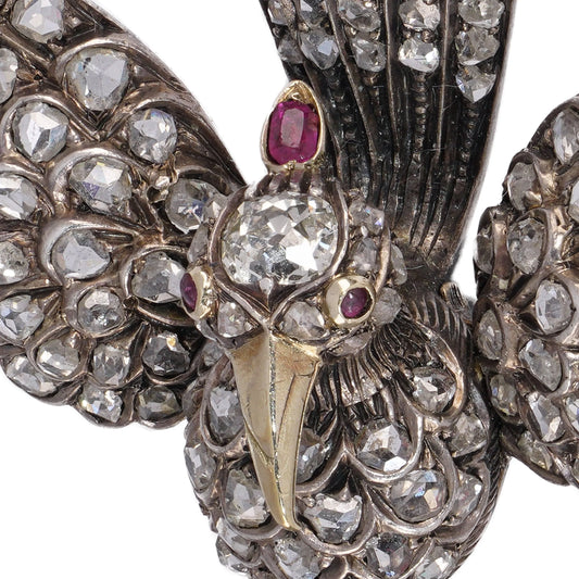 An antique bird in flight brooch set with diamonds and rubies, in silver and gold, on a white background