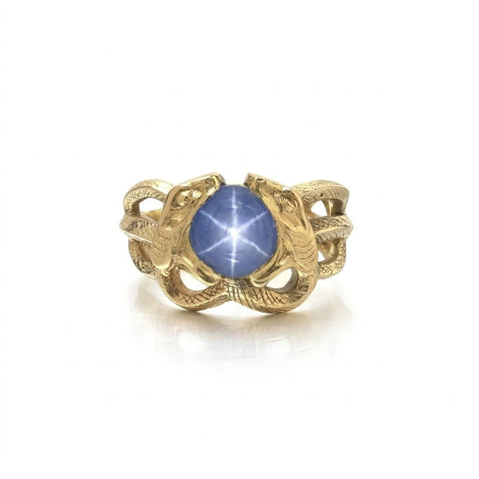 A yellow gold double snake ring holding a cabochon star sapphire in their mouths
