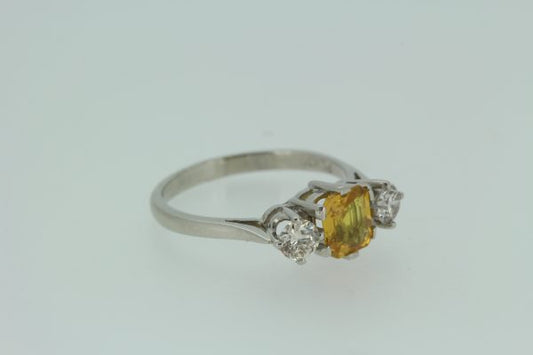 Yellow Sapphire and Diamond Three Stone Ring in Platinum; central 1.25ct octagonal step-cut yellow sapphire flanked by 0.55cts brilliant-cut diamonds