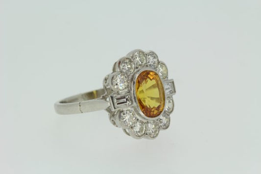 Yellow Sapphire and Diamond Floral Cluster Ring; central 2.50ct oval yellow sapphire within a surround of 1.30cts brilliant-cut diamonds with baguette diamonds shoulders, in platinum