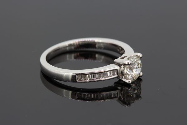 Diamond Solitaire Engagement Ring with Baguette Shoulders; central 0.85 carat round brilliant-cut diamond, claw set, flanked by channel-set baguette-cut diamond set shoulders, in 18ct white gold