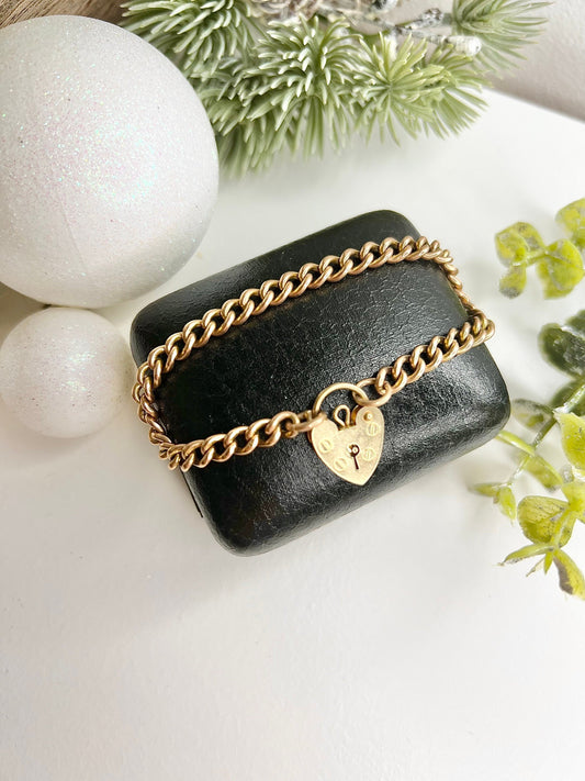 A gold curb link bracelet with a heart-shaped padlock clasp
