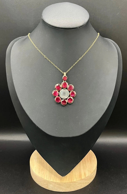 An antique garnet locket pendant in gold, with a chain, on a black bust