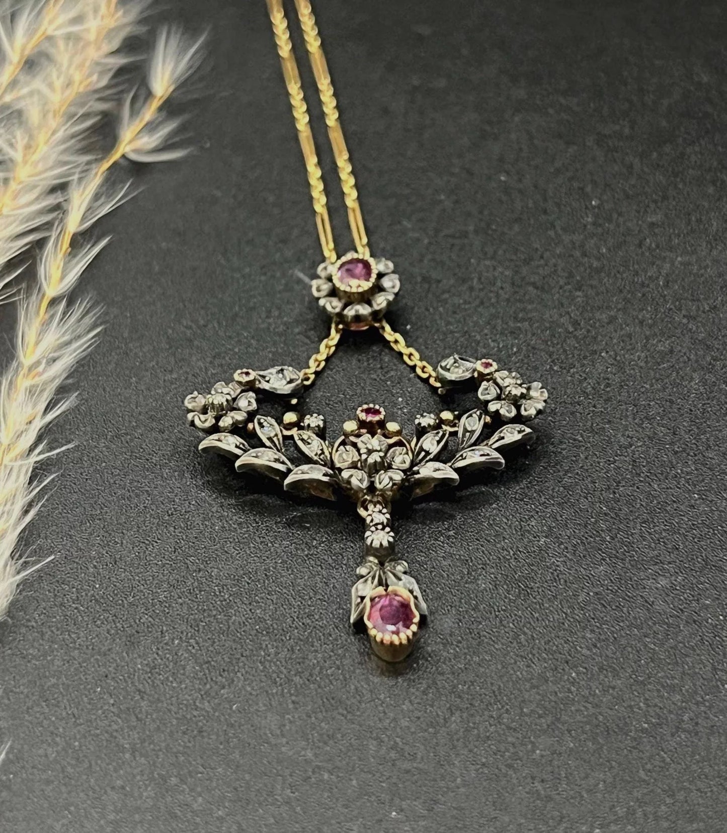 An ornate pendant with rubies and diamonds in gold and silver, with an integrated chain, on a black background