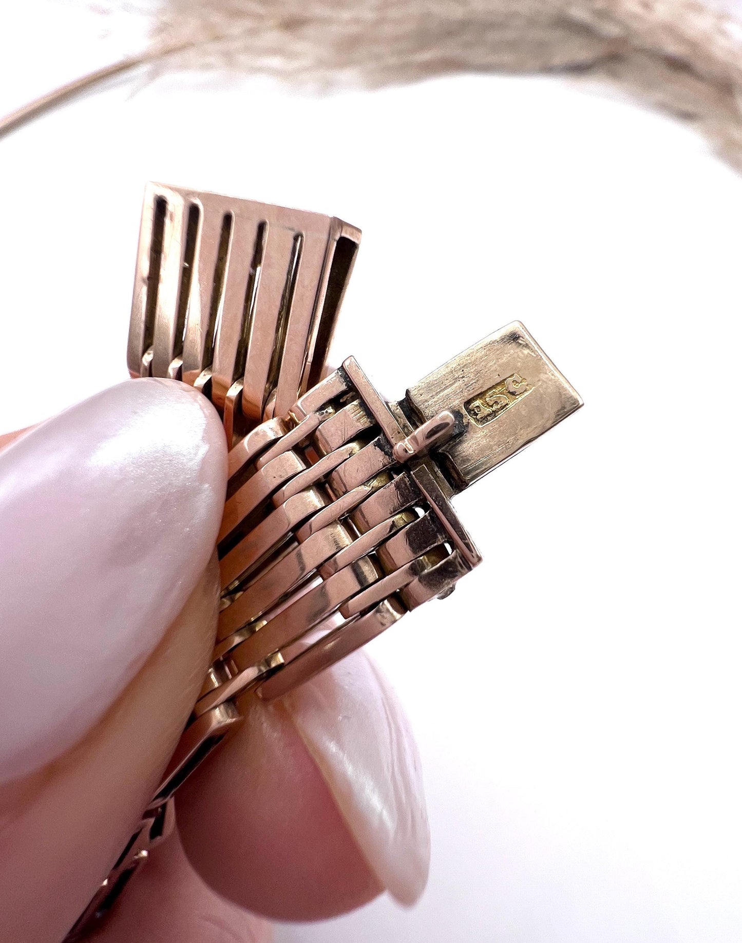 A yellow-rose gold gate style bracelet, held in a hand