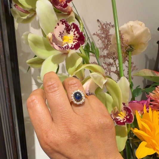 An oval cluster ring with a cabochon sapphire and diamond surround, in yellow gold, modelled on a hand