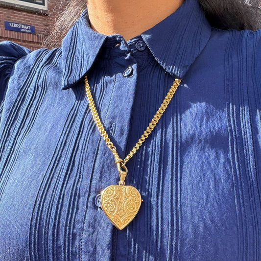 A yellow gold fancy link chain necklace, modelled with a heart pendant by a woman in a blue shirt
