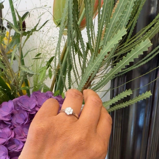 A white gold diamond daisy cluster ring, modelled on a hand