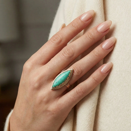 A navette shaped turquoise single stone ring in yellow gold, modelled on a hand