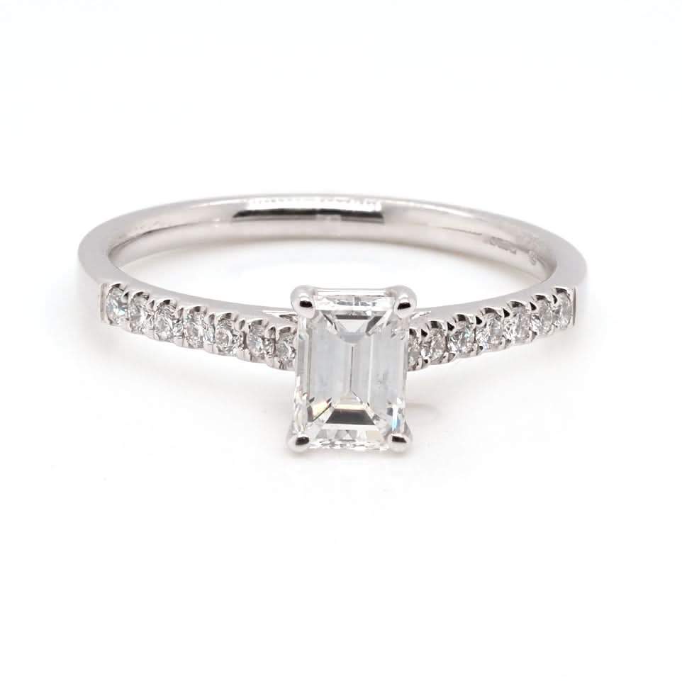 An emerald cut diamond ring in white gold, with diamond set shoulders