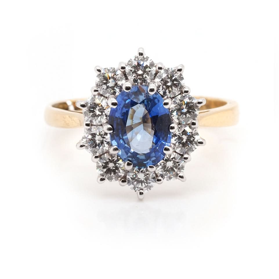 An oval sapphire and brilliant cut diamond cluster ring in yellow and white gold