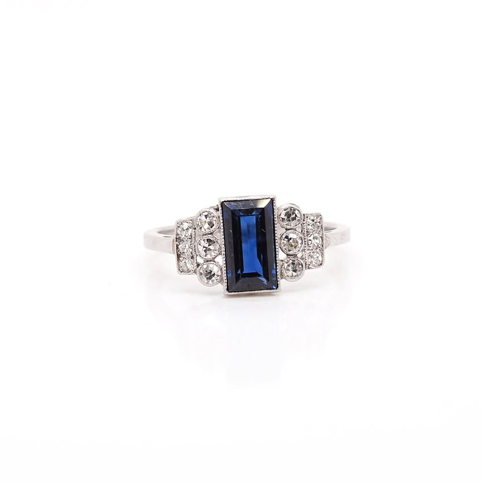 A platinum Art Deco design ring with a central sapphire and diamond set shoulders