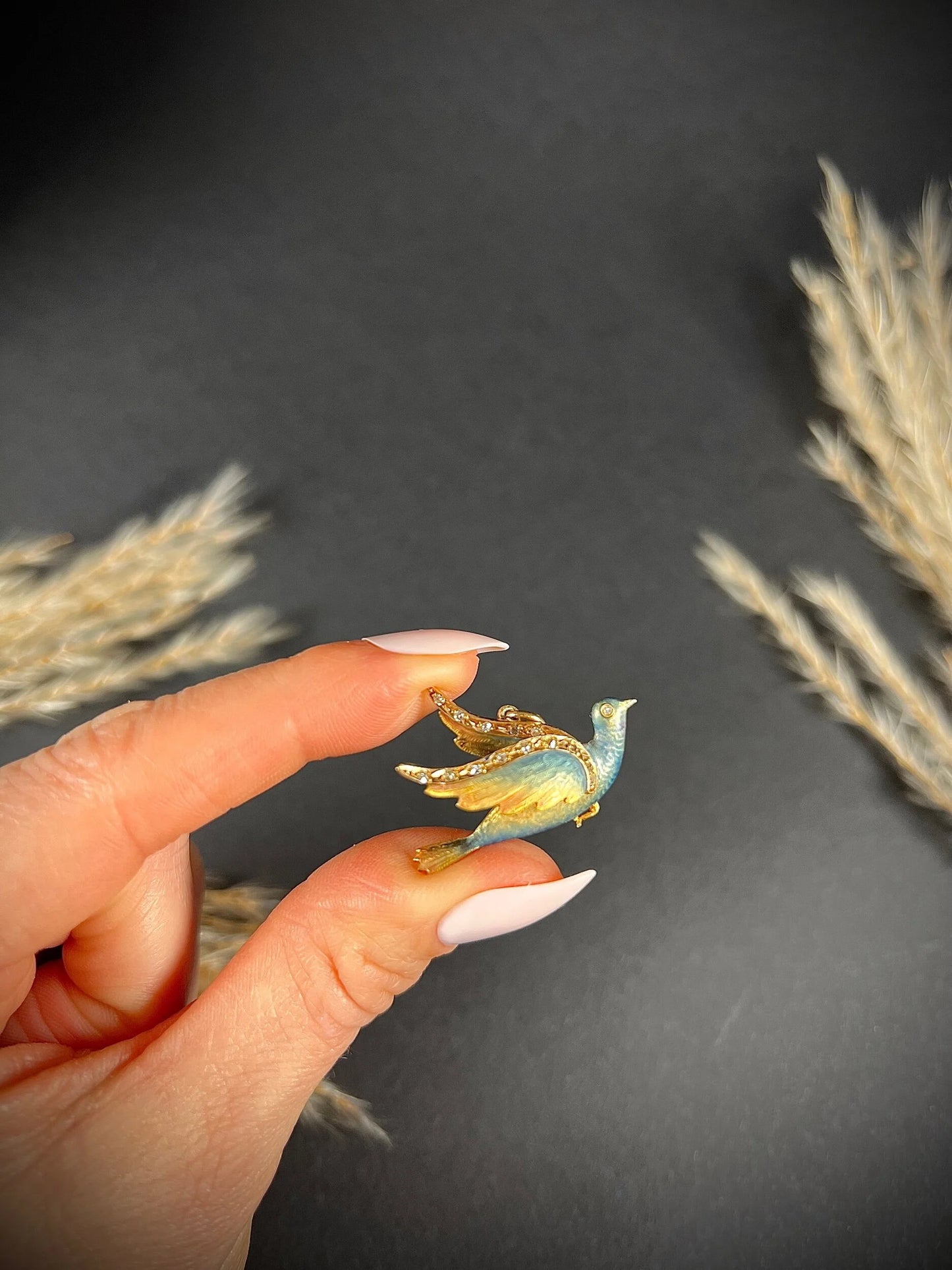 An enamel and diamond dove bird pendant, held in a hand