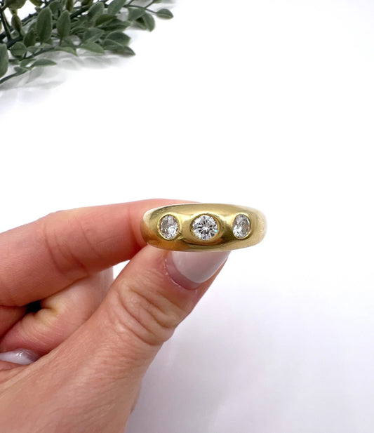 A three stone round diamond yellow gold flush set band ring, held in a hand