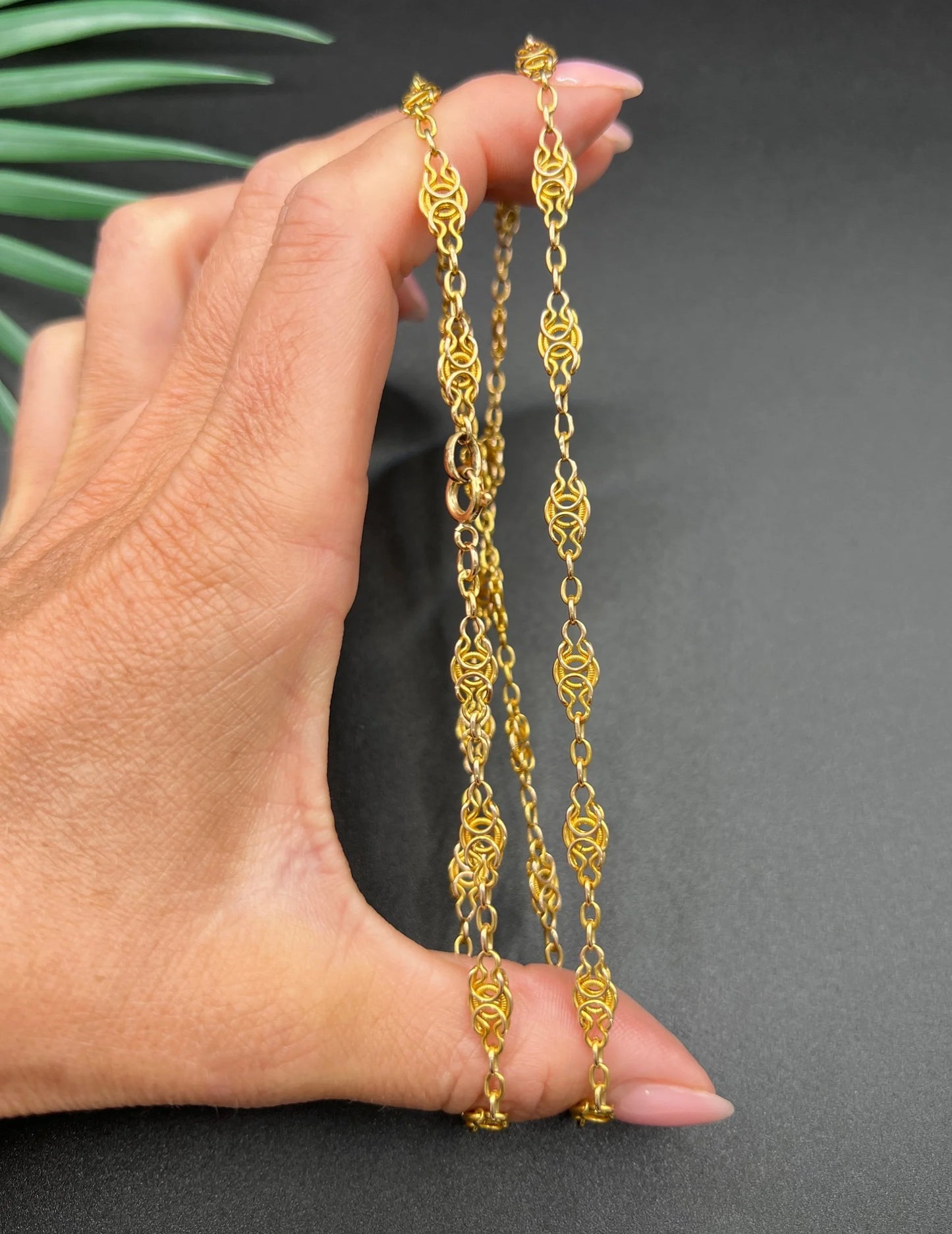 A yellow gold fancy link chain necklace, held in a hand
